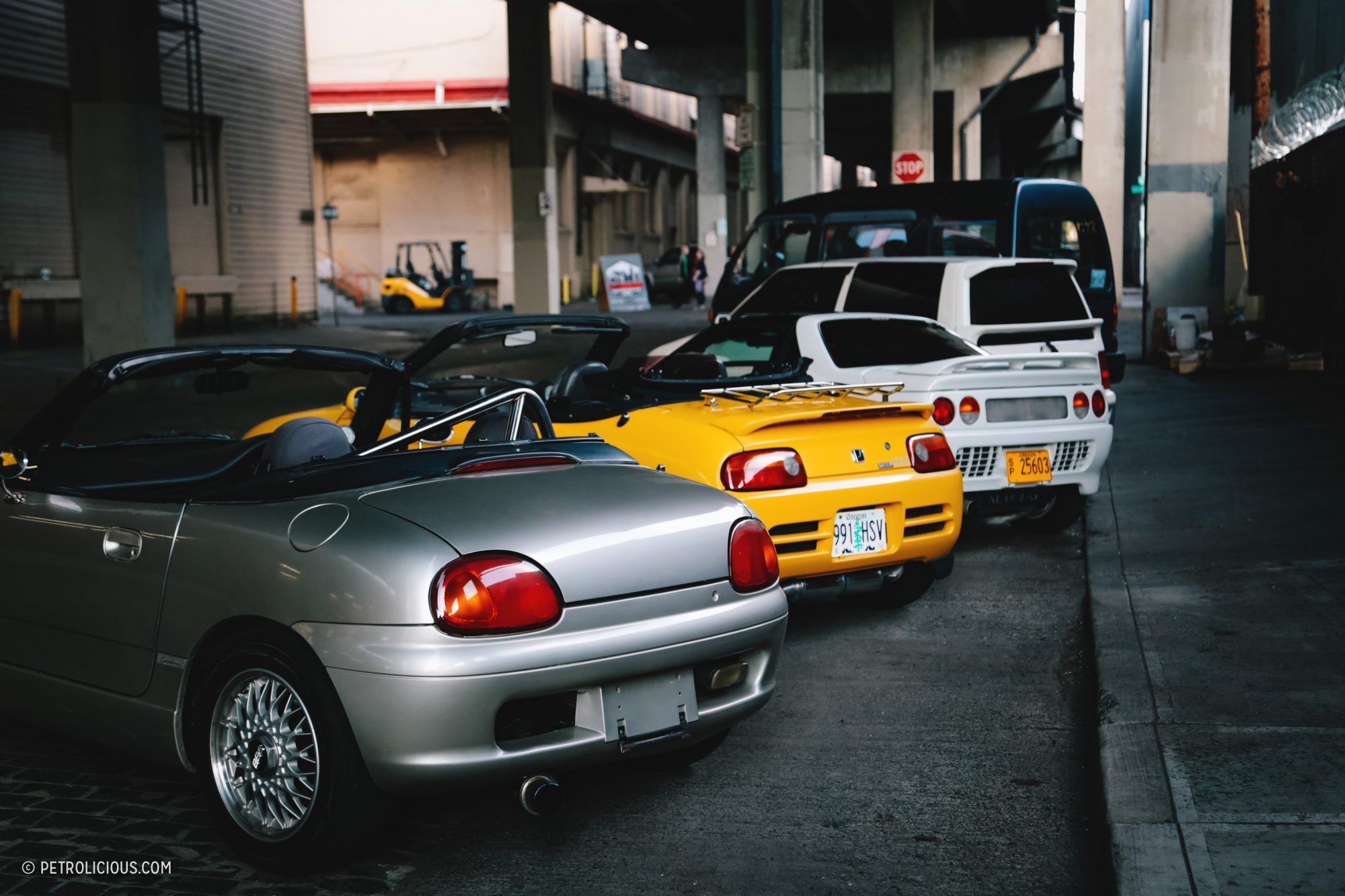 A row of kei cars parked under a concrete structure